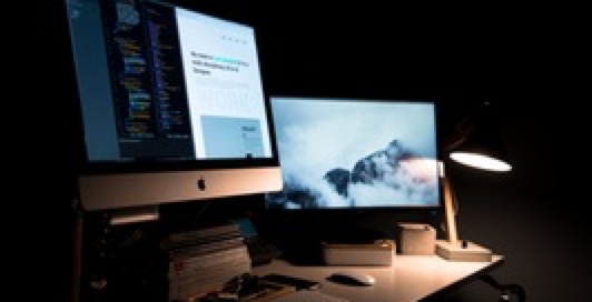 monitors on a desk with a lamp in a dark room